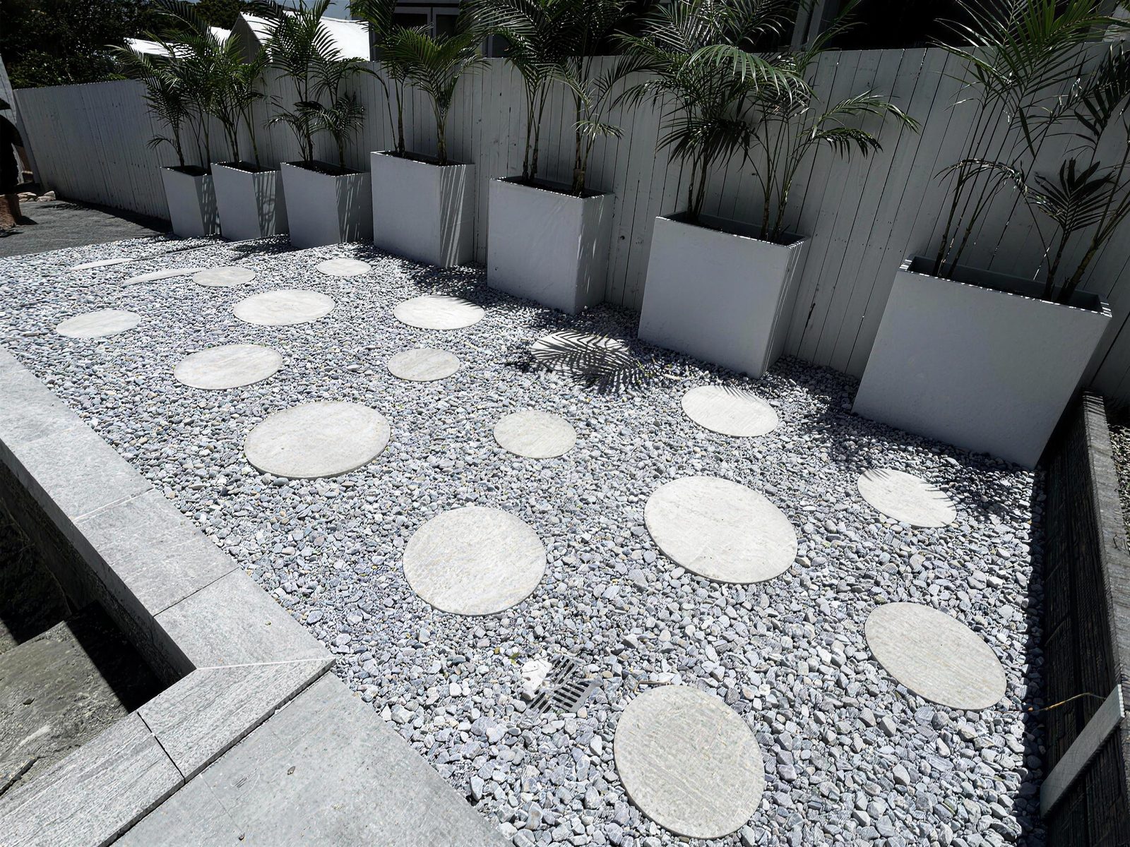 Courtyard with white pebbles, round pavers and palms in planters